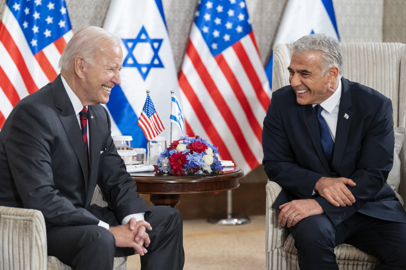 Interim PM Lapid and President Biden sit together with Israeli and American flags in the background.